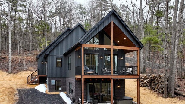 Una cabaña moderna de dos pisos con balcón, ventanas amplias y terraza de madera.