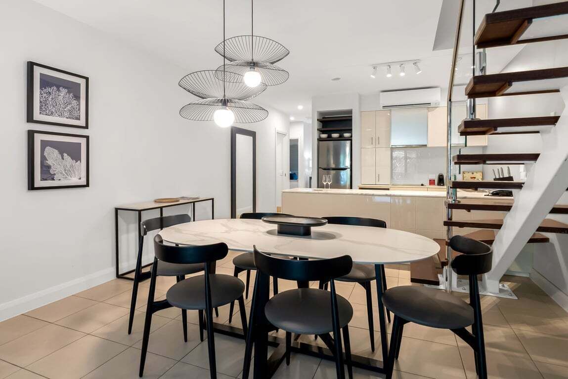 Ein moderner Essbereich mit einem runden Tisch und sechs Stühlen, im Hintergrund eine Küche und eine Treppe mit Holzstufen.