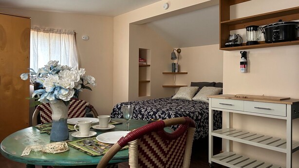 A compact room with a bed, a dining table with chairs, a small kitchen area with shelves, and a ceiling fan. - Rustic 1-bedroom studio in Emigrant near Yellowstone N.P. and Chico Hot Springs (Emigrant)
