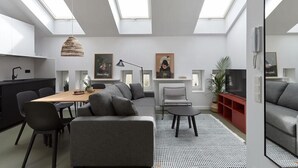 A modern living room with a sofa, dining table, and chairs. There is a TV, a lamp, and artwork on the walls. - Plantonia Aparthotel (Kraków)