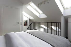 A modern bedroom with skylights, a bed, a staircase, and a painting on the wall. - Plantonia Aparthotel (Kraków)