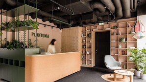 A reception area with a counter, shelving with plants, a chair, and a round table. - Plantonia Aparthotel (Kraków)