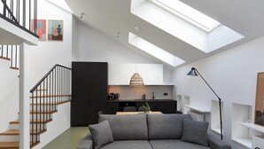 A modern living space with a grey sofa, a staircase with black railings, and a skylight above a kitchen area. - Plantonia Aparthotel (Kraków)