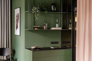 Una cocina con gabinetes verdes, encimera negra y una planta colgante.