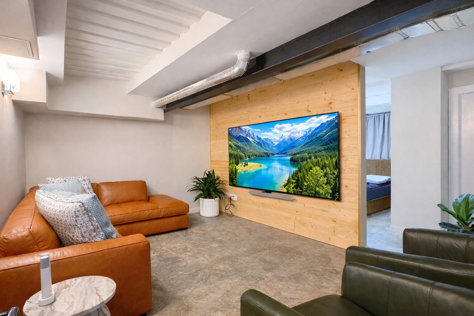 Uma sala de estar moderna com uma grande televisão de tela plana fixada em uma parede de madeira, um sofá de couro marrom, uma pequena mesa redonda e um banco de couro verde.