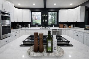 Une cuisine moderne avec des meubles blancs, un îlot central doté d’un plan de travail en marbre, un four en acier inoxydable et une fenêtre offrant une vue sur la verdure à l’extérieur.