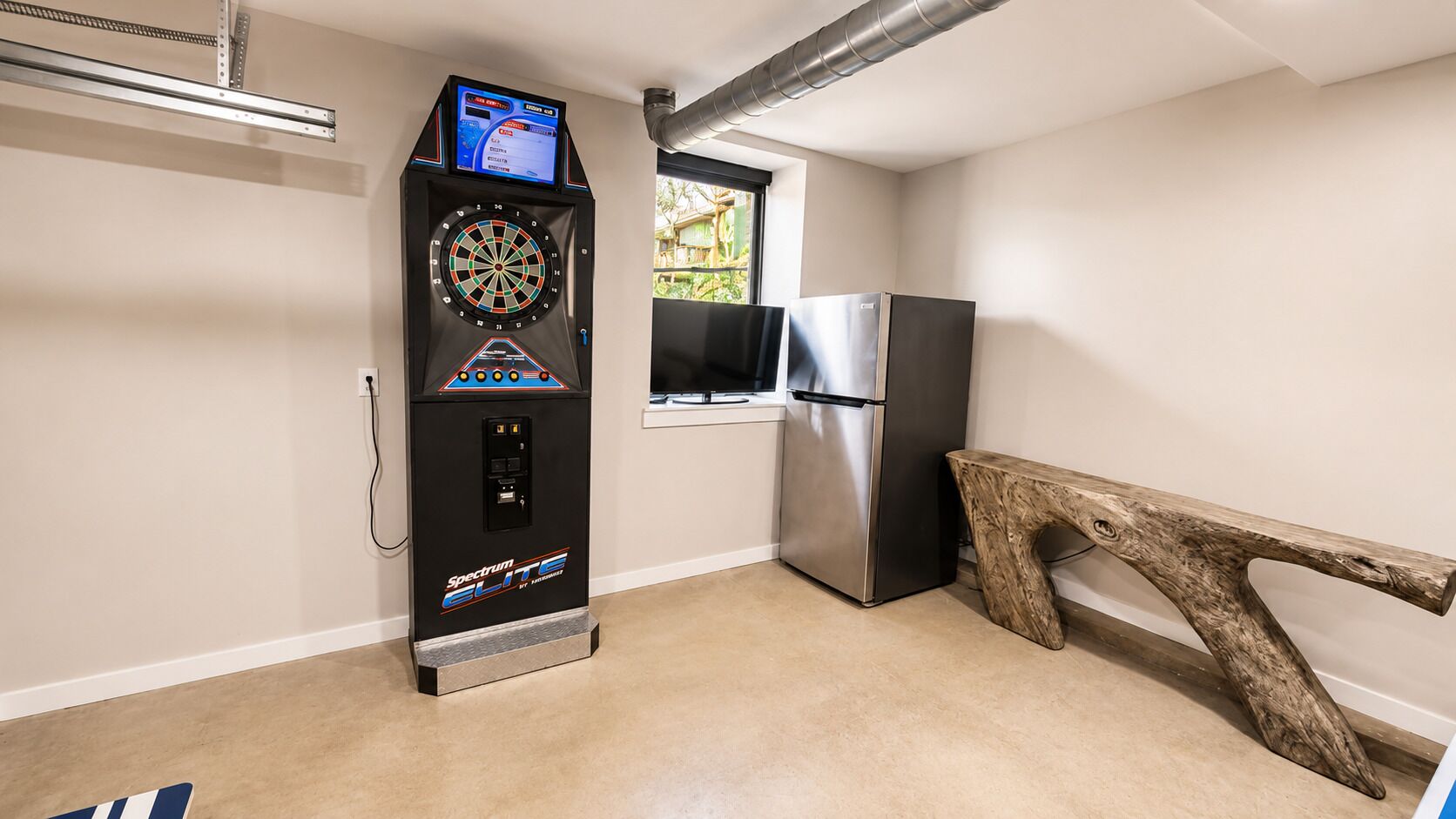 A compact kitchen with a dartboard, a refrigerator, and a wooden bench.