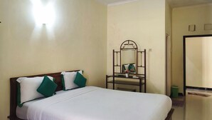 A bedroom with a wooden bed, white bedding, and a green pillow. - Homely Guest House Tegal (Tegal)