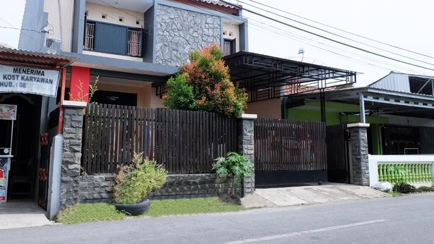 A two-story house with a stone facade, a black metal gate, and a small garden area. - Homely Guest House Tegal (Tegal)