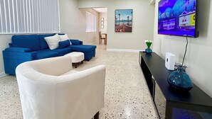 A modern living room with a blue sectional sofa, a white armchair, a coffee table, a flat-screen TV mounted on the wall, and a small table with a vase. - Family Home in the Heart of Miami (Miami)