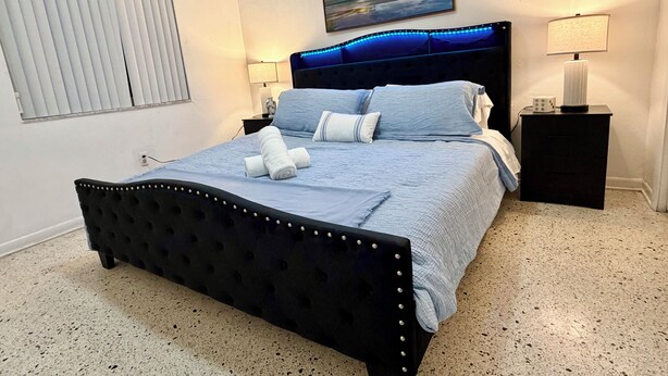 A neatly made bed with a blue bedspread and white towels, a black upholstered headboard, and a painting above the bed. - Family Home in the Heart of Miami (Miami)