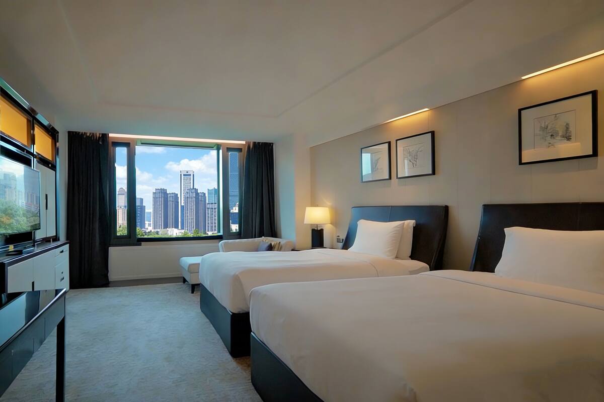 Een hotelkamer met twee bedden, een bureau, een televisie en een raam met uitzicht over de stad.