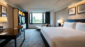 A hotel room with a large bed, a desk with a computer, a chair, a sofa, and a TV. - The Grand Mansion Hotel (Nanjing)