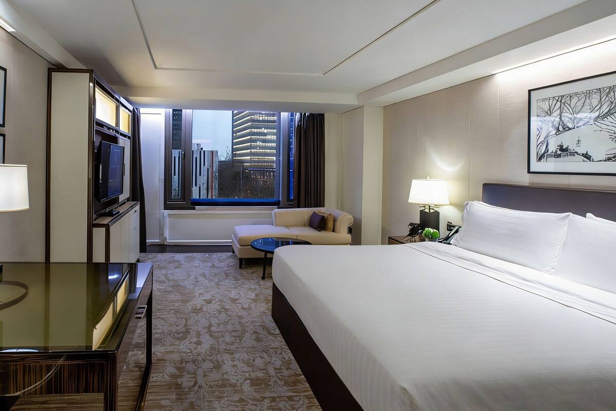 Hotelkamer met een bed, bureau, televisie, sofa, klein tafeltje en een raam met uitzicht op de stad.