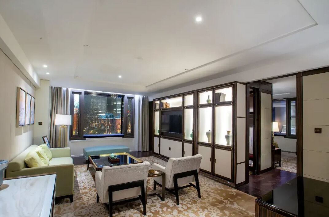 A modern hotel room with a city view, a sofa, a coffee table, and a TV.