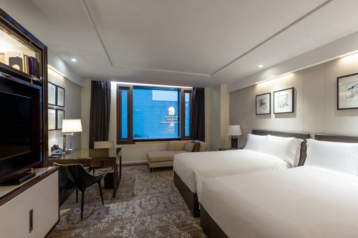 Een hotelkamer met twee bedden, een bureau met stoel, een televisie en een raam met gordijnen.