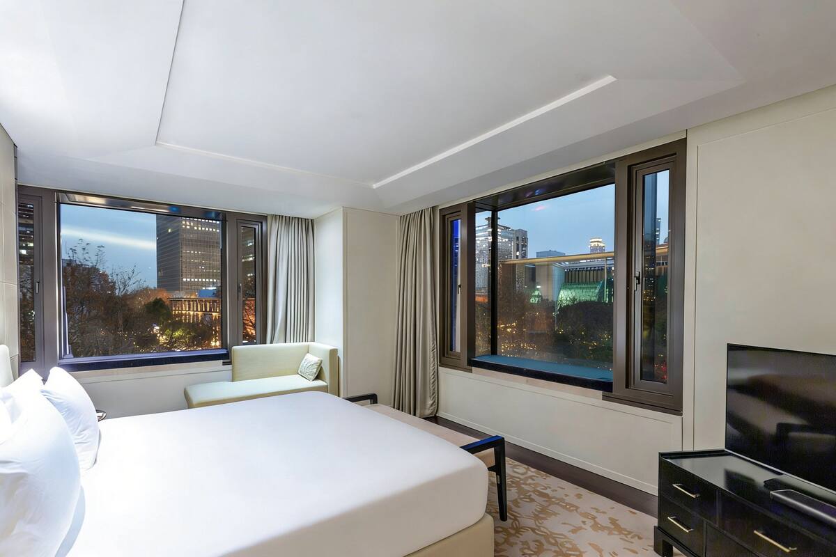 Hotelkamer met een groot bed, een televisie, een bureau en uitzicht op de stad door grote ramen.