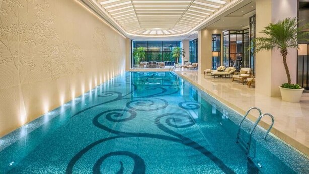 An indoor swimming pool with a glass ceiling, lounge chairs, and a view of the outdoors. - The Grand Mansion Hotel (Nanjing)
