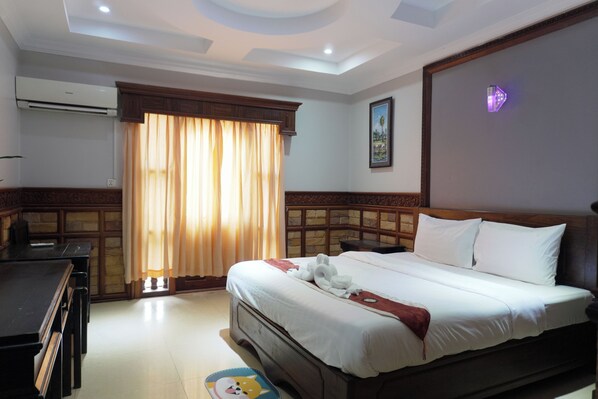 A hotel room with a bed, a desk, a chair, an air conditioner, a window with curtains, and a wall-mounted light fixture. - Dara Panha Sak Guesthouse (Siem Reap)