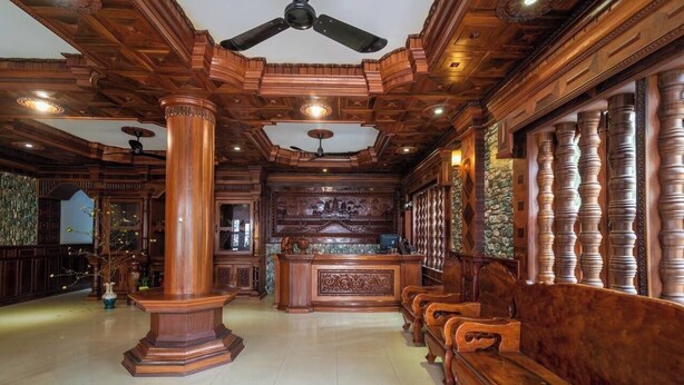 Een ruime lobby met hoge houten plafonds, een centraal gelegen receptiebalie en een rij houten banken langs de muur.