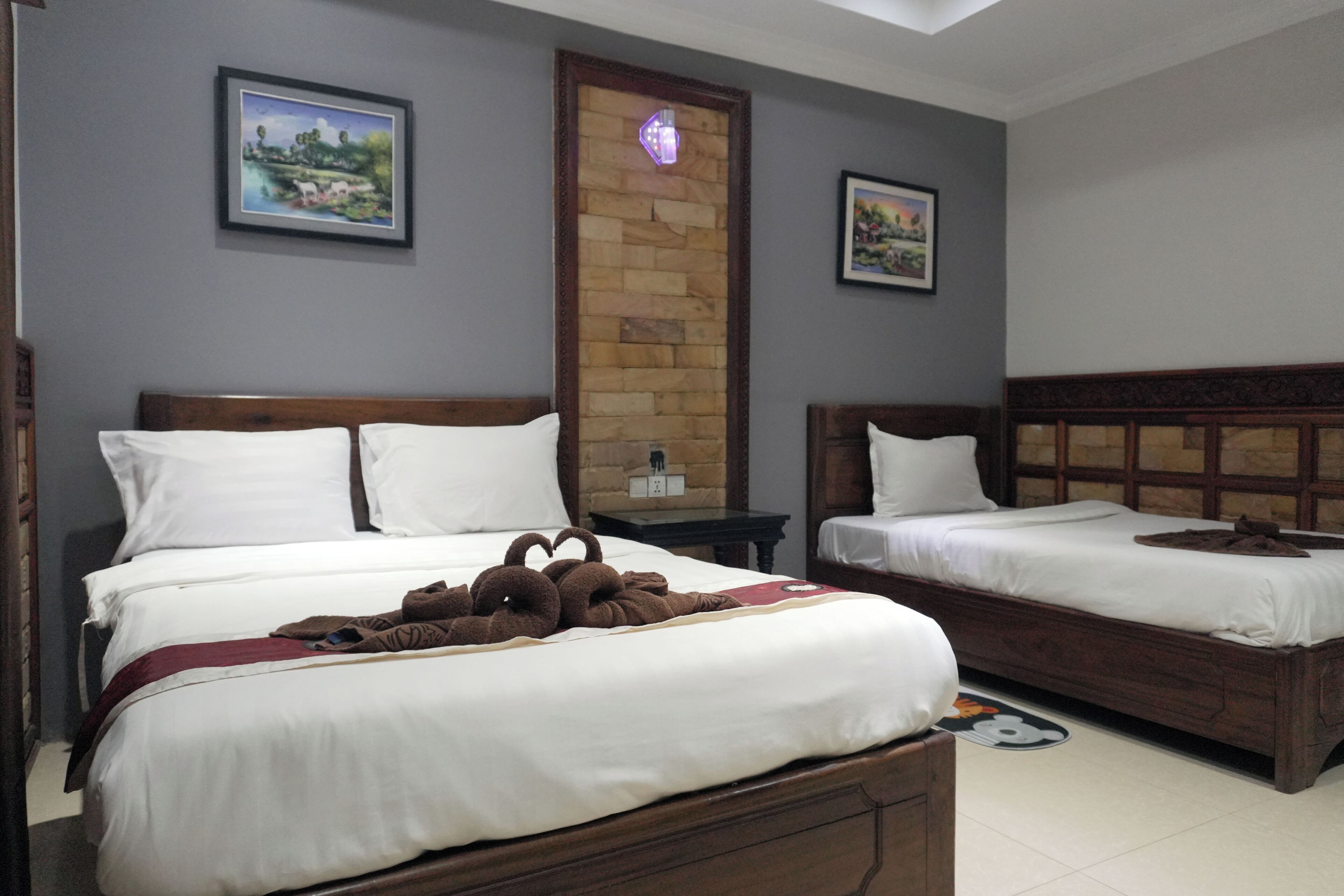 A hotel room with two beds, a wooden headboard, a nightstand, and a wall-mounted light fixture.