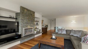 A modern living room with a stone fireplace, a flat-screen TV, and a grey sofa. - Catalina Apt 1 - amazing views and walk to town (Queenstown)