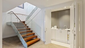 Eine moderne Treppe mit Glastrennstäben und Holzbeschlägen, die zu einem Küchenbereich mit weißen Schränken und einer eingebauten Spüle führt.