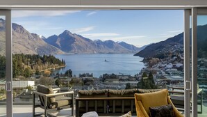 Ein modernes Zimmer mit einem großen Glasfenster, das einen malerischen Blick auf einen See, Berge und eine Stadt freigibt.