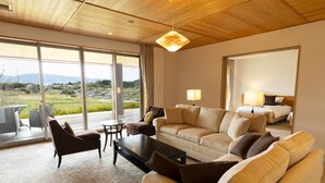 A spacious living room with a large sofa, a coffee table, and a TV. There is a balcony with a view of the countryside. - AUBERGE de SENVIE (Sakurai)