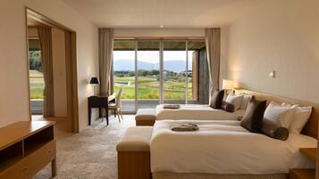 A hotel room with two beds, a desk, and a view of a green landscape.