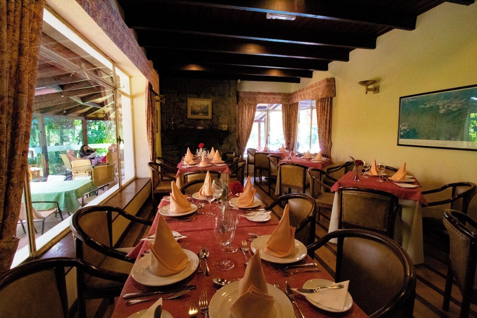 A restaurant with tables set for dining, featuring a view of the outdoors through large windows.