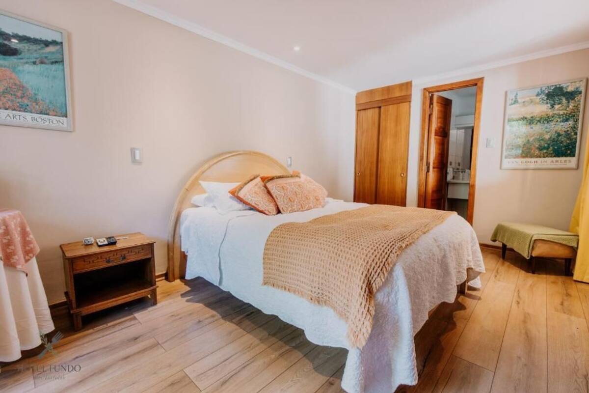 A bedroom with a wooden bed, a nightstand, a bench, and a door leading to another room.