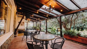 Un patio couvert avec des tables et des chaises rondes, des poutres en bois et une vue sur la verdure.