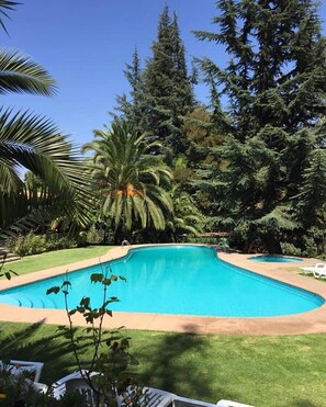 A swimming pool surrounded by lush greenery and tall trees. - Hotel Fundo Las Tórtolas (Limache)