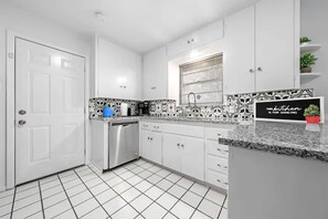 A modern kitchen with white cabinets, a stainless steel dishwasher, a black and white patterned backsplash, and a sign that reads 'This kitchen is for dancing.' - Vibrant 3/2 Remodel w/ Full Size Twister & Disc Golf Gameroom Fun (Temple)