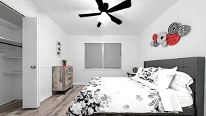 Un dormitorio con cama, ventilador de techo, ventana, armario y cómoda.