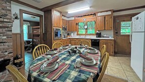 Uma cozinha acolhedora com armários de madeira, uma mesa de jantar posta para quatro pessoas e uma geladeira.