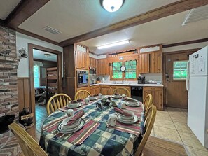 A cozy kitchen with wooden cabinets, a dining table set for four, and a refrigerator. - Creekside Cottage- Fishing Cabin (Bryson City)