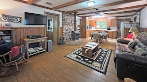 Uma sala de estar ampla com lareira, vigas de madeira, televisão e área de jantar com mesa e cadeiras.