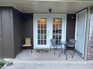 A front door with a glass panel, a small porch with two wicker chairs and a table, and a doormat with a lion's head design. - 3-bedroom townhome in fantastic Kansas City with AC (Kansas City)