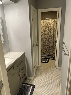 A bathroom with a white sink, a mirror, a door leading to a hallway with a marble floor. - 3-bedroom townhome in fantastic Kansas City with AC (Kansas City)