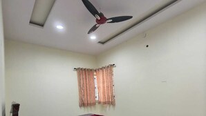 Un dormitori amb llit, ventilador al sostre, finestra amb cortines i terra de rajola.