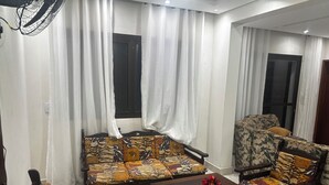 A living room with a sofa, chairs, a coffee table, and a fan. - Beautiful and cozy duplex with private pool. (Guarujá)