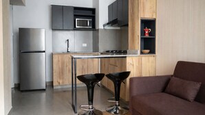 A modern kitchen with a stainless steel refrigerator, a microwave, and a gas stove. There are two black bar stools and a brown sofa in the living area. - Modern, comfortable and centrally located apartment (Lima)