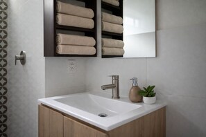 Ein Badezimmer mit einem weißen Waschbecken, einem modernen Wasserhahn und einem Regal mit ordentlich gefalteten Handtüchern.
