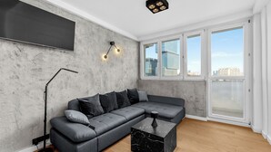Un salon moderne avec un canapé d’angle, une table basse en marbre, une lampe sur pied et une grande fenêtre donnant sur la ville.
