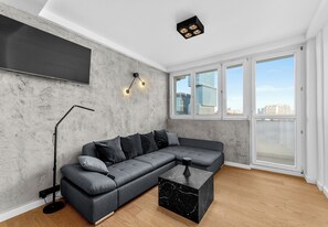 Ein modernes Wohnzimmer mit einer Eckcouch, einem Marmortisch, einer Stehlampe und einem großen Fenster mit Blick auf die Stadt.
