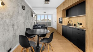 Une cuisine moderne avec des meubles en bois, un coin repas doté d’une table ronde et de chaises, et une grande fenêtre offrant une vue sur la ville.