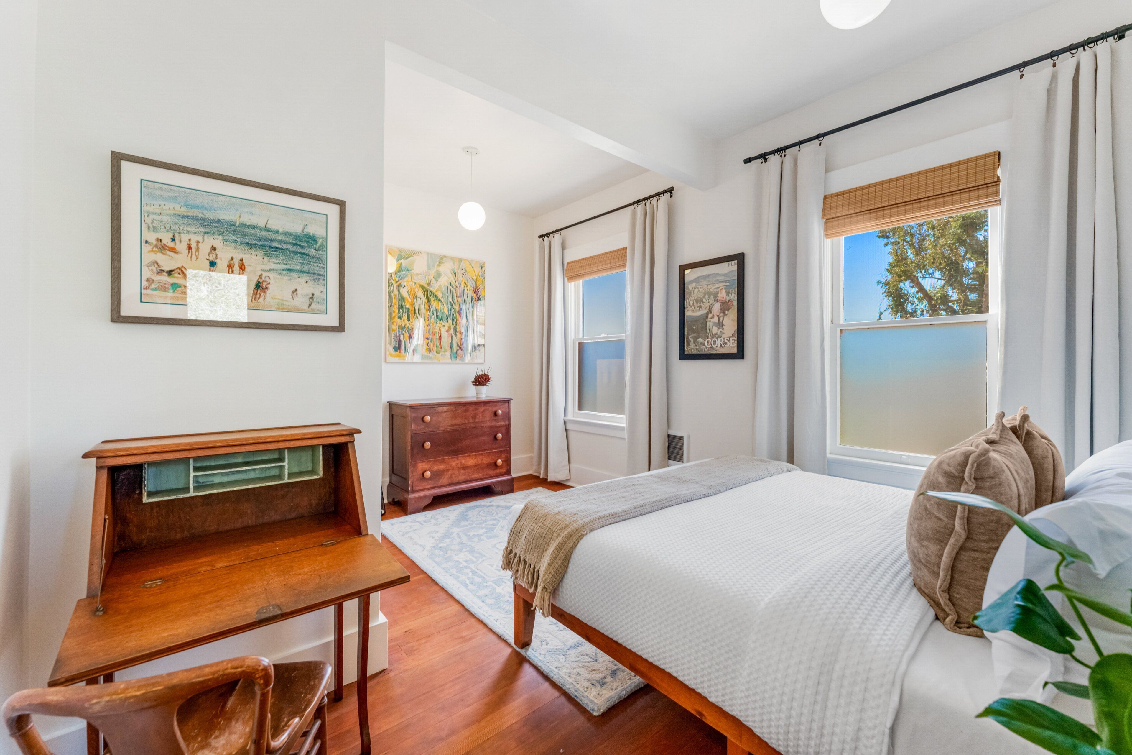Un dormitorio con cama, escritorio, cómoda y ventana con cortinas.