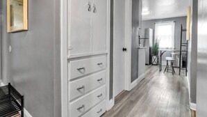 A hallway with a white wardrobe, a small table with two stools, and a refrigerator in the background.